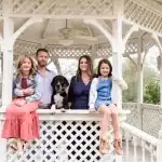 Smiling family with dog in white gazebo.