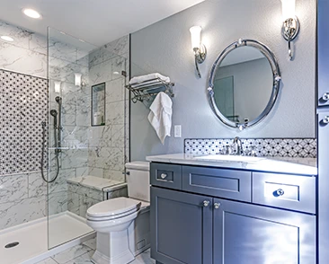 Modern bathroom with a glass shower, marble tile, round mirror, and blue vanity.