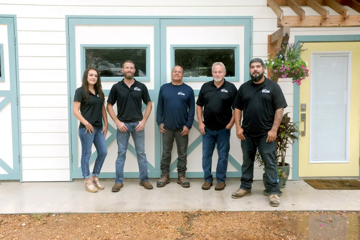 Team of five standing in front of a white and teal building, smiling at the camera.